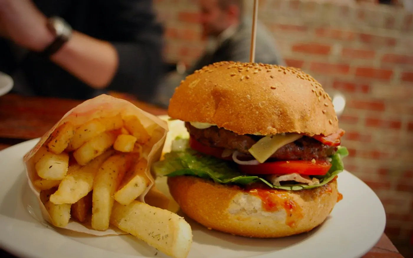 Hamburguesa doble con queso derretido y tocino, iluminada a contraluz sobre fondo oscuro