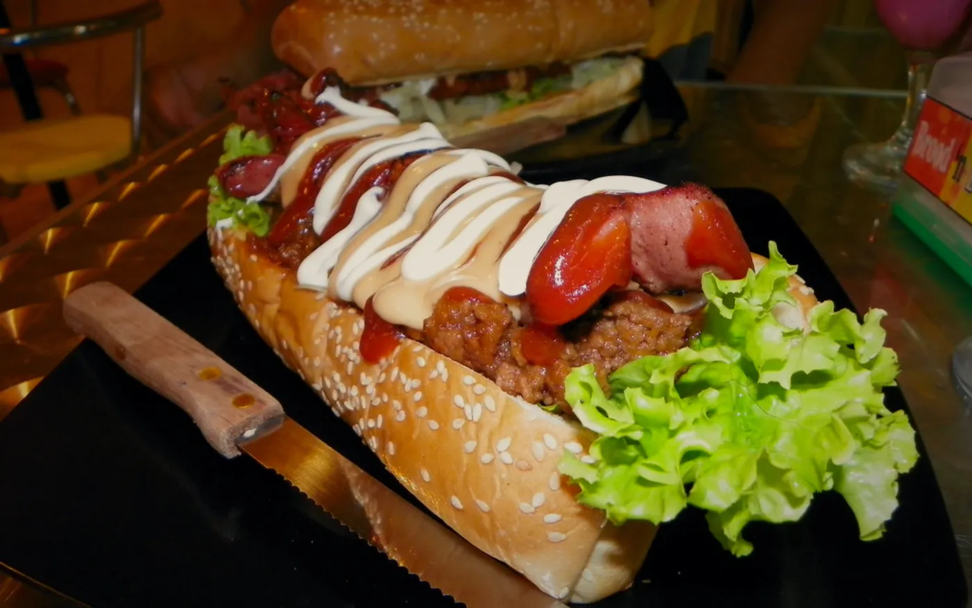 Hot dog cargado con tocino, guacamol y jalapeños sobre plato oscuro